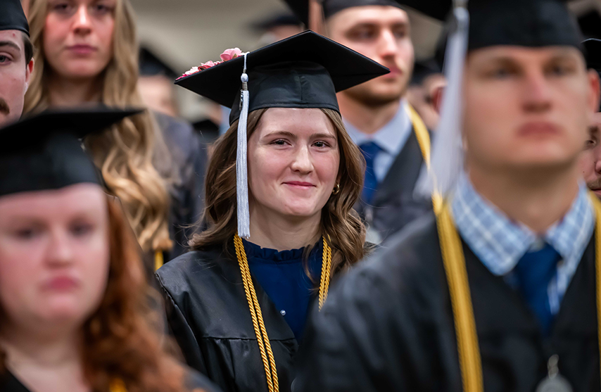 A young woman smiles into the camera, dressed in commencement regalia.