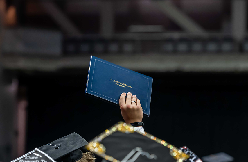 A recently graduated student holds their degree up in triumph.