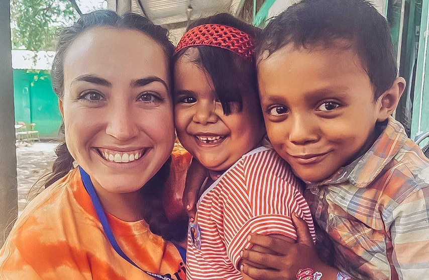 Una mujer con playera naranja se toma una selfie dos niños.