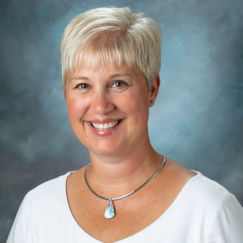 Kris Burt smiles into the camera against a blue background.